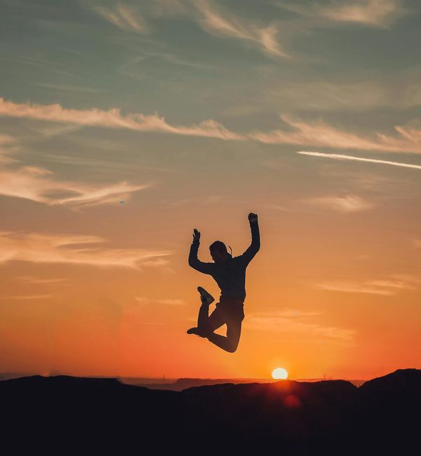 Silhouette of a person jumping with joy against a stylized sunrise.